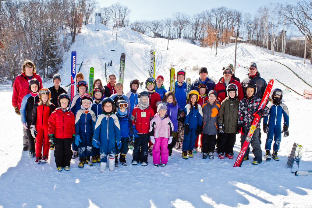 Group of people and children with snow suits and skis standing on a snowy hill